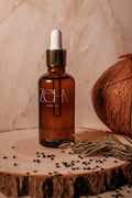Zehn Hair Oil bottle on a wooden surface with coconut, rosemary, and black seed. Lightweight botanical hair and scalp oil handcrafted in Canada.