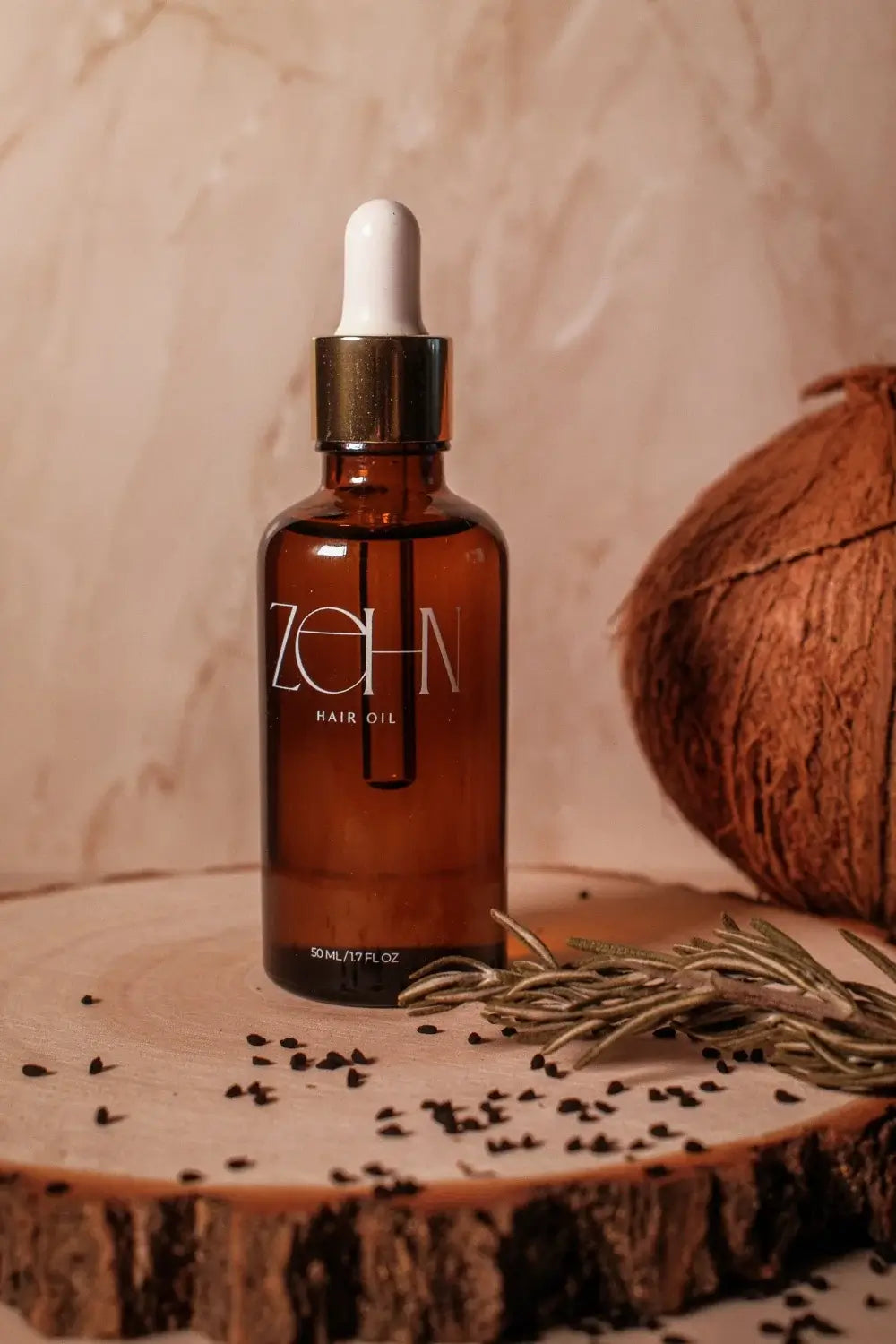 Zehn Hair Oil bottle on a wooden surface with coconut, rosemary, and black seed. Lightweight botanical hair and scalp oil handcrafted in Canada.